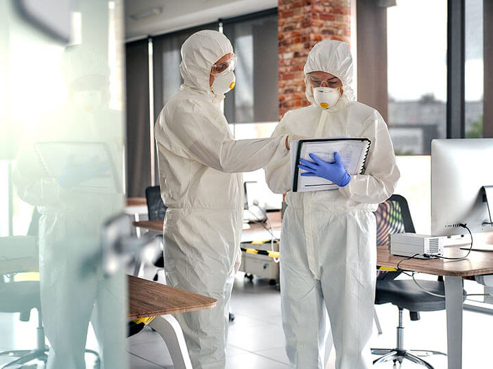 People people in protective white suits, masks, and glasses talking while looking at a notebook in an office space